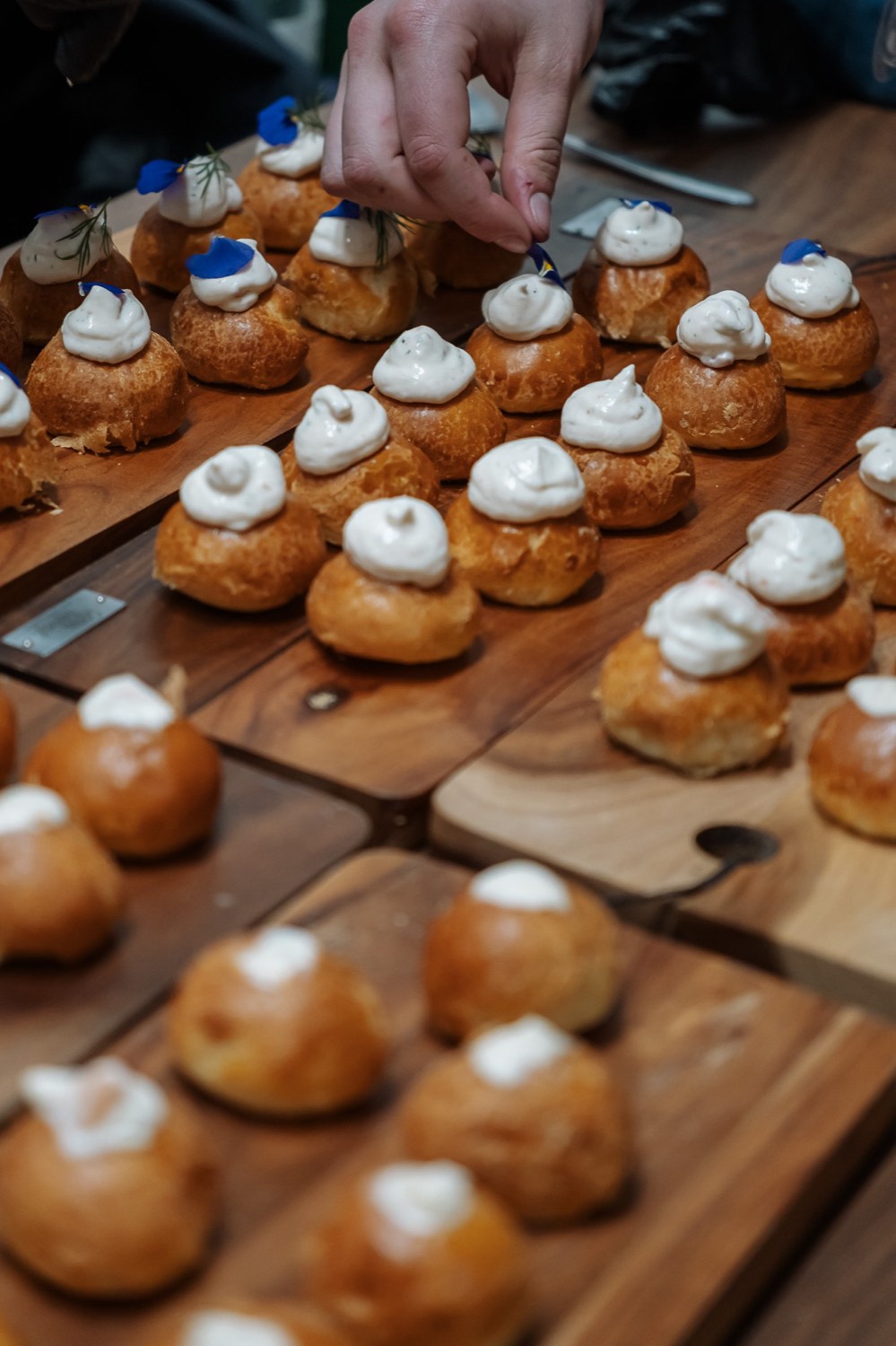 Hartige soesjes met een toef crème en een blauw bloemblaadje op houten planken