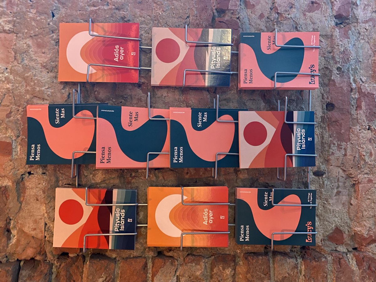 Postkaarten van Lucy's met Piensa menos, siente más in een rekje tegen de bakstenen muur