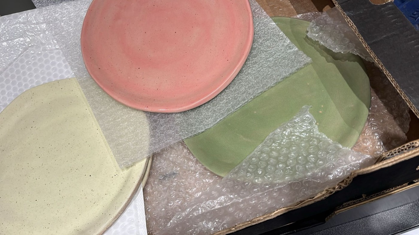 Handgemaakte borden in roze, groen en zandkleur, net uitgepakt uit noppenfolie