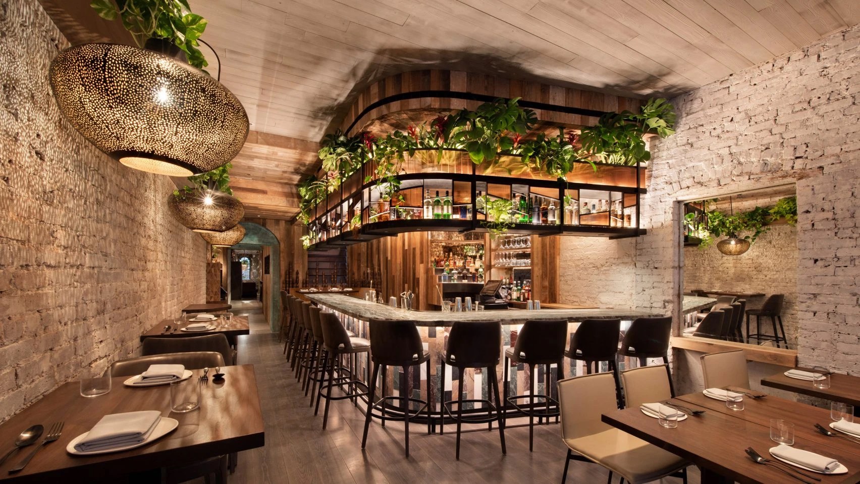De bar van Wayan met planten boven de toog, houten wanden en grote koperen lampen